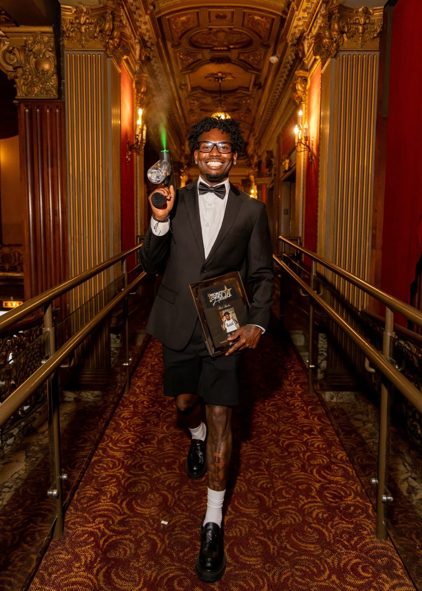 Sly Huncho holding a People's Choice Best Barber award in an ornate theater hall